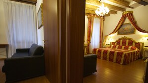 Una habitación con piso de madera, un sofá de color oscuro, una cama con cubrecama rojo y dorado, y un candelabro.