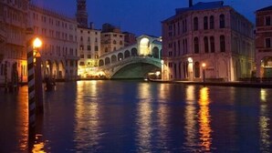 Un puente histórico sobre un canal, flanqueado por edificios iluminados por farolas.