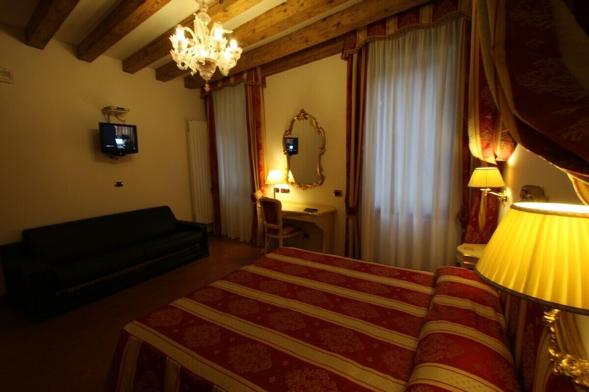 Una habitación de hotel con cama, escritorio, silla, televisor, espejo y candelabro.