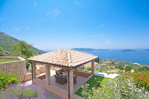 Un espacio de estar al aire libre techado, con vista al mar y colinas.