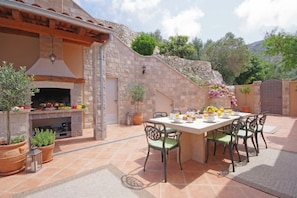 An outdoor dining area with a stone wall, a grill, and potted plants.