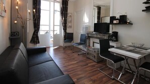 Una sala de estar moderna con un sofá de cuero negro, una mesa de comedor con sillas, un televisor y una chimenea.