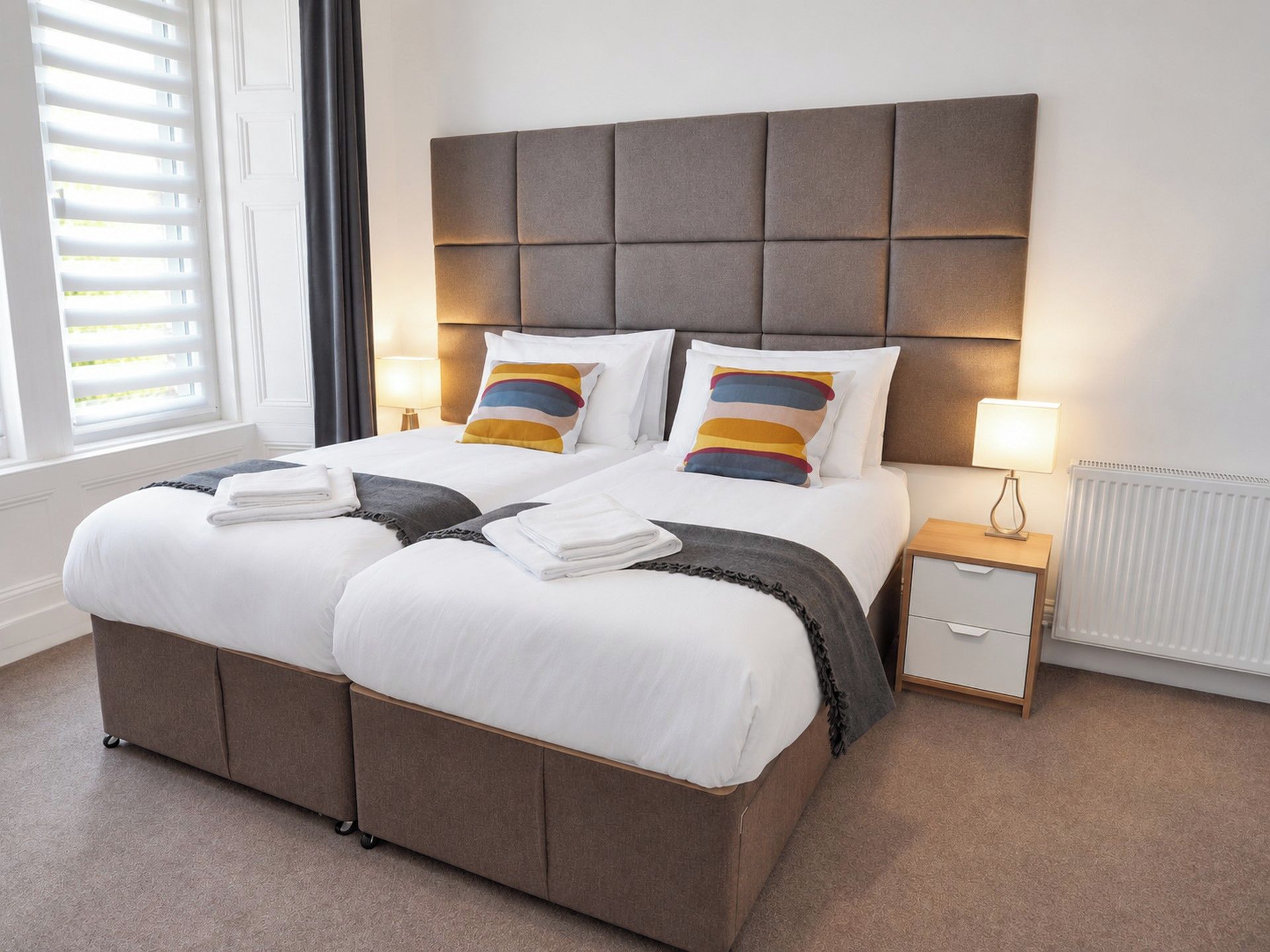 A double bed with a padded headboard, two bedside tables with lamps, and a radiator.