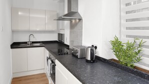 A modern kitchen with white cabinets, a black countertop, stainless steel appliances, and a plant. - Baxter Park City Base (Dundee)