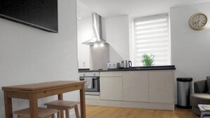 A modern kitchen with a wooden table and stools, a stainless steel range hood, and a small island with a toaster and kettle. - Baxter Park City Base (Dundee)