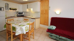 A compact kitchen with white cabinets, a dining table with chairs, a red sofa, and a wooden door. - Mont-Dore: 2-room Apartment near Thermal Baths, Sleeps 4 (Mont-Dore)