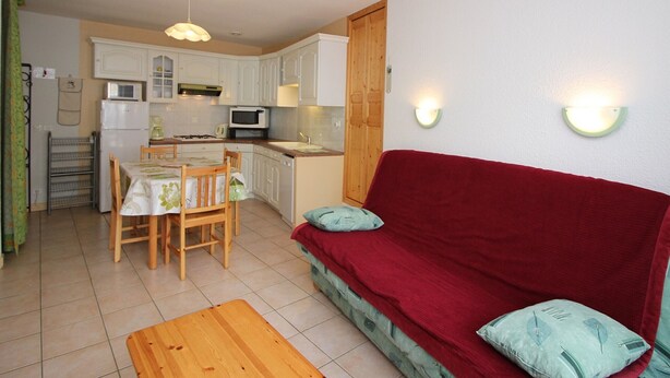 A compact living space with a kitchenette, a dining area, and a red sofa with cushions. - Mont-Dore: 2-room Apartment near Thermal Baths, Sleeps 4 (Mont-Dore)