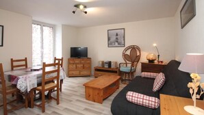 A furnished living room with a sofa, a wooden coffee table, a TV on a wooden cabinet, and a dining area with chairs and a table. - Central T2 near spa with wifi (Mont-Dore)