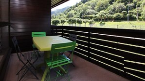 A balcony with a table and chairs, overlooking a forested hillside. - Mont-Dore: 1BR with Balcony, Covered Parking, 4 pax (Mont-Dore)