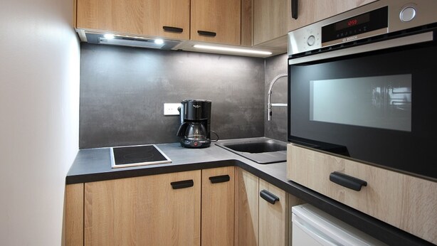 A modern kitchen with wooden cabinets, a built-in oven, a coffee maker, and a dishwasher. - Mont-Dore: 1BR with Balcony, Covered Parking, 4 pax (Mont-Dore)
