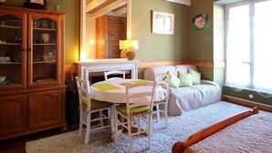 A bedroom with a bed, a dining table with chairs, a wooden cabinet, a mirror, and a window. - Charming city center studio with wifi (Mont-Dore)