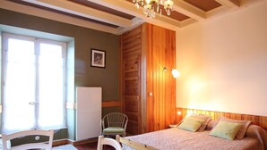 A bedroom with a bed, a chair, a table, and a refrigerator. - Charming city center studio with wifi (Mont-Dore)
