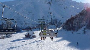 A ski lift with chairs moving up a snowy slope, a mountain in the background, and a clear sky. - Charming city center studio with wifi (Mont-Dore)