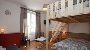 Una stanza con un letto a castello, una scrivania, una sedia, un comò rosso e una finestra con tende.