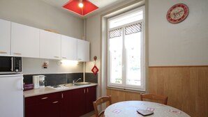 Una cucina compatta con mobili bianchi, un forno a microonde e un lavandino. C'è un tavolo da pranzo con sedie e un orologio appeso al muro.