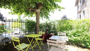 Een terras met gele en witte stoelen en tafels, omringd door groen en een stenen muur.