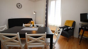 Een moderne woonkamer met een eettafel, witte stoelen, een zwarte bank, een televisie en een kamerbehang.