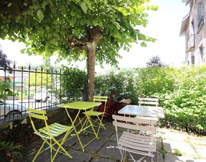 Un espace extérieur aménagé avec des chaises et des tables jaunes et blanches, entouré de verdure et d’un mur en pierre.