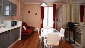 A compact kitchen with a microwave, a dining table with chairs, a red sofa, and a large mirror. - Charming 1BR in Mont-Dore for 4, city center (Mont-Dore)