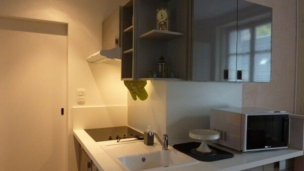 A modern kitchen with a white countertop, a sink, a microwave, and a clock on the wall. - Charming 1BR in Mont-Dore for 4, city center (Mont-Dore)