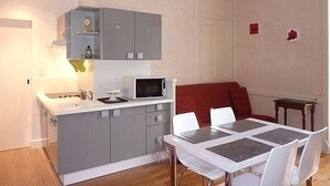 A compact kitchen with a microwave, a sink, and grey cabinets. There is a dining area with a white table and chairs. - Charming 1BR in Mont-Dore for 4, city center (Mont-Dore)