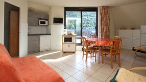A compact living space with a kitchenette, dining area, and a balcony with a view of greenery.