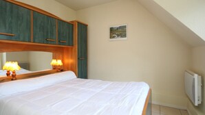 A bedroom with a bed, wooden headboard, two bedside lamps, a small picture on the wall, and a radiator.