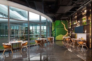 Un intérieur moderne avec des murs en verre, une fresque murale verdoyante et des meubles en bois.