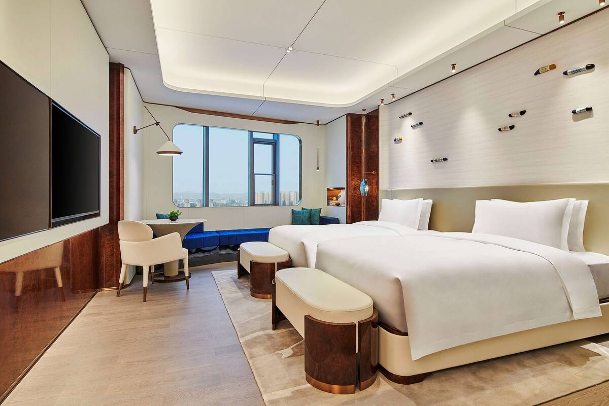 A modern hotel room with a large bed, a desk, and a view of the city.
