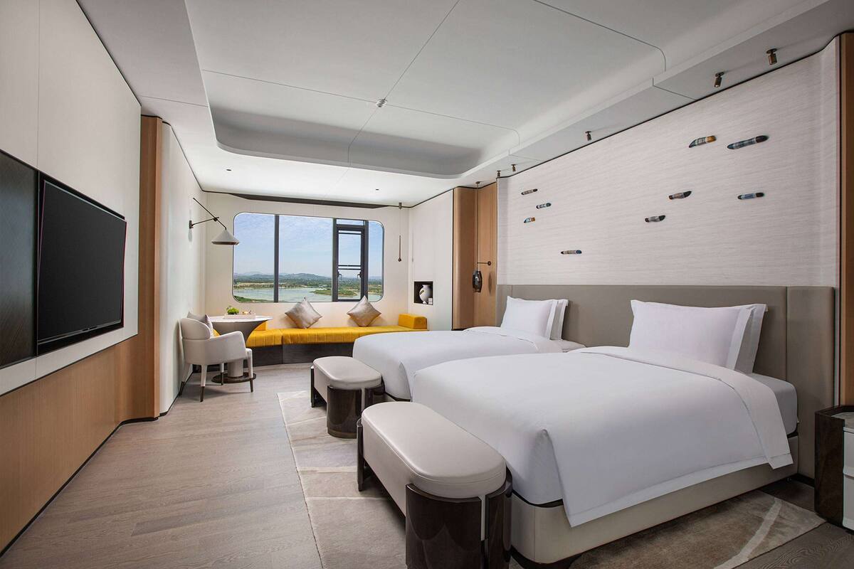 A modern hotel room with two beds, a seating area with a view, and a flat-screen TV.