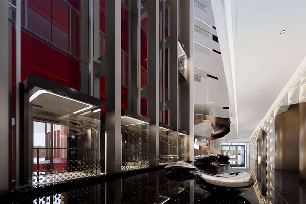 Un intérieur d’hôtel moderne avec un ascenseur en verre, des surfaces réfléchissantes et un mur d’accent rouge.