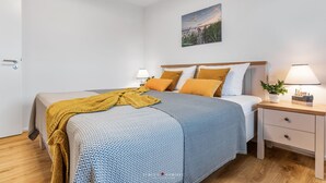 Une chambre à coucher bien rangée, avec un lit, des tables de chevet et une lampe fixée au mur.
