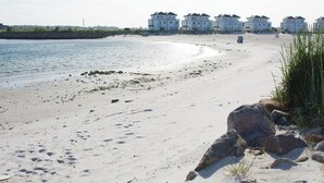 Une plage de sable avec de gros rochers et quelques bâtiments en arrière-plan.