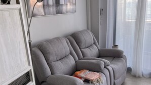 Ein graues Sofa mit einer Decke und Kissen, eine weiße Kommode und ein Bild an der Wand.