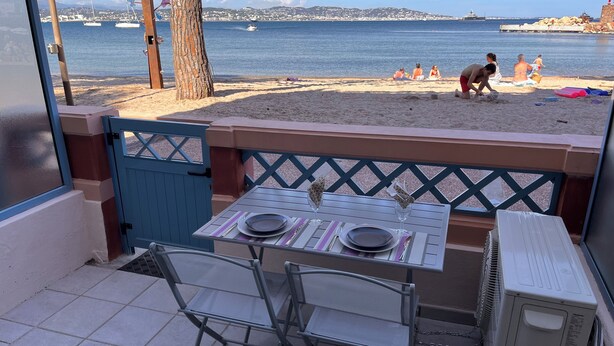 Ein Balkon mit Tisch für zwei Personen, mit Blick auf einen Strand mit Menschen und Booten.