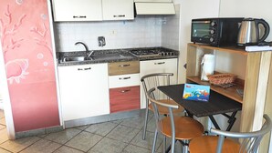 Una cucina compatta con mobili bianchi, un piano di lavoro in granito, un lavello, un fornello, un microonde e un piccolo angolo ristoro con tavolo e sedie.