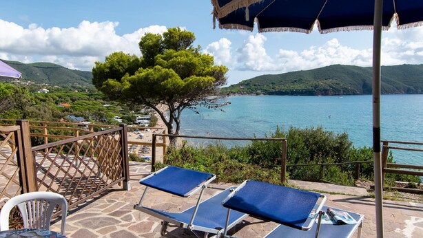 Una terrazza con due poltrone blu, un parapetto in legno e vista su una zona costiera con alberi e un corso d'acqua.