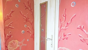 Una stanza con una porta, le pareti decorate con un motivo simile al corallo e con creature marine.
