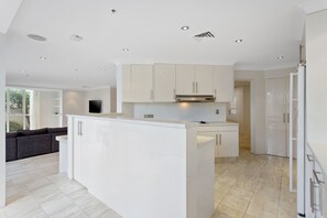 A modern kitchen with white cabinetry, a central island, and recessed lighting. - Spacious 3 Bedroom Family Apartment (Surfers Paradise)