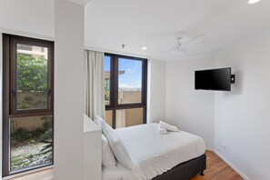 A bedroom with a bed, a TV mounted on the wall, and a view of the outdoors through a window. - Spacious 3 Bedroom Family Apartment (Surfers Paradise)
