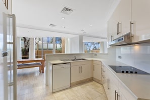 A modern kitchen with a dishwasher, a sink, and a stove. There is a bench and a view of the outdoors through a window. - Spacious 3 Bedroom Family Apartment (Surfers Paradise)