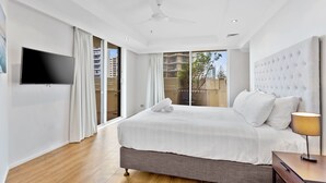 A modern hotel room with a large bed, a flat-screen TV, and a view of the city through large windows.