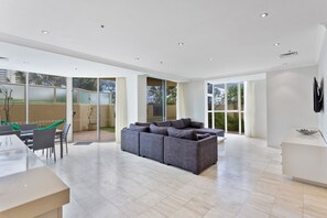 Amplia sala de estar con un sofá seccional gris, una mesa de comedor con sillas y ventanas grandes que ofrecen vistas al exterior.
