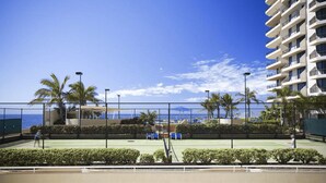 A tennis court with a view of the ocean and a high-rise building in the background.
