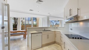 A modern kitchen with a dishwasher, sink, and stove. There is a bench and a view of palm trees outside.