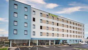 Un hotel de varios pisos con fachada plana, amplias ventanas y estacionamiento.
