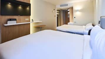 A hotel room with a flat-screen TV mounted on the wall, a bed with white bedding, a bedside table, and a small shelf with a remote control.