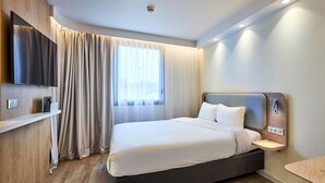 A modern hotel room with a large bed, a mounted TV, a bedside table, and a window with curtains. - B&B HOTEL Deauville-Touques (Touques)