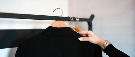 A hand holding a black garment on a wooden hanger against a wall with a black horizontal bar.