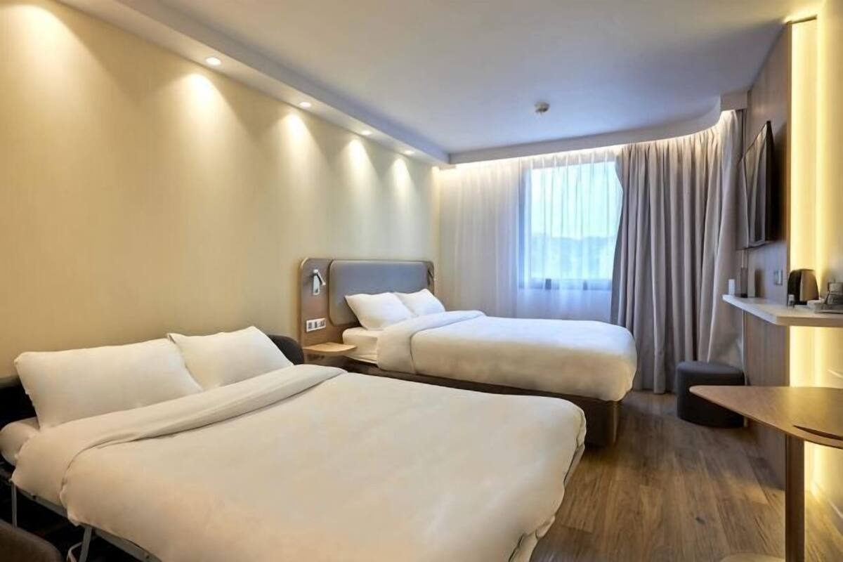 A hotel room with two beds, a desk, a TV, and a window with curtains.